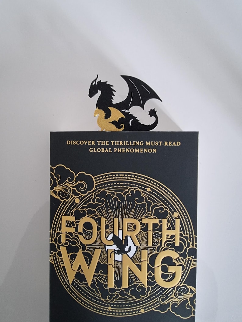 May include: A black and gold book cover with the title "Fourth Wing" in gold lettering. The cover features a stylized dragon design with clouds and a circle.