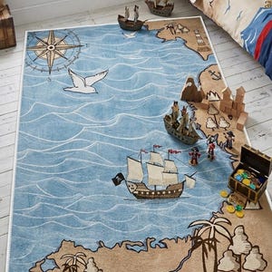 May include: A rectangular area rug featuring a printed pirate map design with a blue ocean, tan landmasses, a compass rose, palm trees, a skull, and sailing ships. The rug has a white border and depicts a nautical scene with waves and islands.
