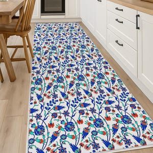May include: A long, rectangular kitchen rug with a white background and a repeating pattern of blue, teal, and red floral and bird motifs. The rug is placed on a light wood floor in a kitchen setting.