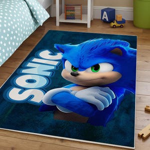 Könnte beinhalten: Ein rechteckiger blauer Teppich mit der Figur Sonic the Hedgehog. Das Wort "SONIC" ist in Weiß und Hellblau dargestellt. Sonic wird mit blauem Fell, grünen Augen und weißen Handschuhen dargestellt. Der Teppich liegt auf einem Holzboden.