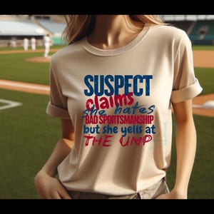 May include: A beige t-shirt with the text "SUSPECT claims she hates BAD SPORTSMANSHIP but she yells at THE UMP" in blue and red lettering.