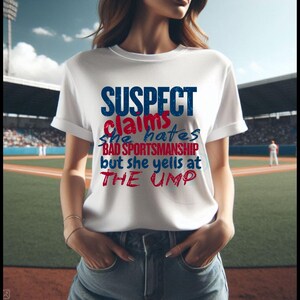 May include: White t-shirt with a blue and red graphic that says "SUSPECT claims she hates BAD SPORTSMANSHIP but she yells at THE UMP"