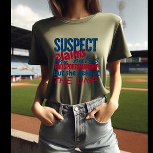 May include: A green t-shirt with the text "SUSPECT claims she hates bad sportsmanship but she yells at THE UMP" in blue, red, and white lettering.