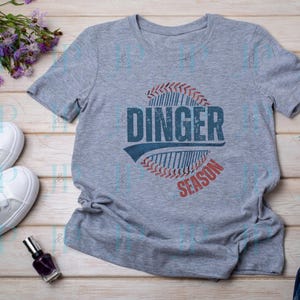 May include: Gray t-shirt with a red, white, and blue baseball graphic and the text "Dinger Season".