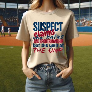 May include: A beige t-shirt with the text "SUSPECT claims she hates BAD SPORTSMANSHIP but she yells at THE UMP" in red and blue lettering.