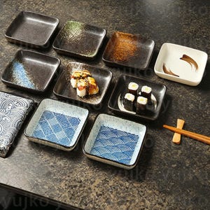 Peut inclure: Un ensemble de dix petites assiettes carrées en céramique avec différents motifs bleus et blancs. Les assiettes sont parfaites pour servir des sushis ou d'autres petites collations.