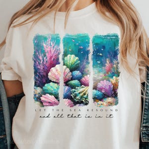 May include: White t-shirt with a colorful seashell and coral design. The text "Let the sea resound and all that is in it" is printed below the design. The verse "Psalm 96:11" is printed in the top right corner of the design.