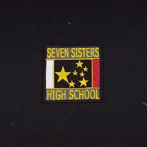 May include: A yellow and black embroidered patch with the text "SEVEN SISTERS HIGH SCHOOL". The patch features a black rectangle with a white and red stripe on each side. Inside the rectangle are seven yellow stars.