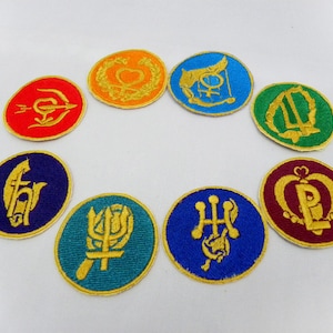 May include: Nine embroidered patches with different designs and colors. Each patch features a gold outline and a unique symbol in the center. The symbols include a heart, a crown, a trident, a sword, a feather, a lyre, a crescent moon, and a staff.