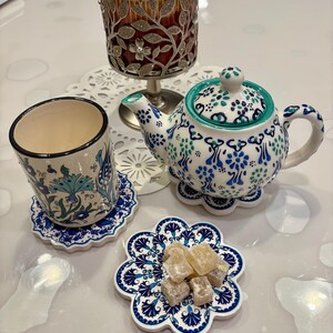 K&ouml;nnte beinhalten: Eine wei&szlig;e Teekanne mit blauen und gr&uuml;nen Blumenmustern, eine wei&szlig;e Tasse mit einem blauen und gr&uuml;nen Blumenmuster und eine wei&szlig;e Untertasse mit einem blauen und gr&uuml;nen Blumenmuster. Es gibt auch ein paar St&uuml;cke gelber S&uuml;&szlig;igkeiten auf einer wei&szlig;en Untertasse mit einem blauen und gr&uuml;nen Blumenmuster.