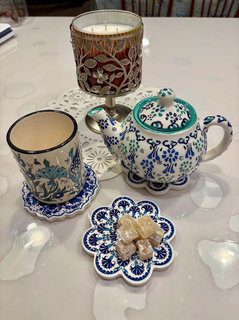 K&ouml;nnte beinhalten: Eine wei&szlig;e Teekanne mit blauen und gr&uuml;nen Blumenmustern, eine wei&szlig;e Tasse mit einem blauen und gr&uuml;nen Blumenmuster und eine wei&szlig;e Untertasse mit einem blauen und gr&uuml;nen Blumenmuster. Es gibt auch ein paar St&uuml;cke gelber S&uuml;&szlig;igkeiten auf einer wei&szlig;en Untertasse mit einem blauen und gr&uuml;nen Blumenmuster.