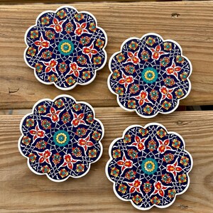 K&ouml;nnte beinhalten: Vier Keramik-Untersetzer mit einem blauen, roten, gelben und gr&uuml;nen floralen Muster. Die Untersetzer sind rund und haben einen gewellten Rand.
