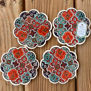 K&ouml;nnte beinhalten: Set aus vier Keramik-Untersetzern mit komplizierten floralen und geometrischen Mustern in Rot-, Blau-, Gr&uuml;n- und Wei&szlig;t&ouml;nen. Die Untersetzer sind handgefertigt in der T&uuml;rkei und tragen ein Etikett mit der Aufschrift "Handmade in Turkey, Fait &agrave; la main en Turquie".