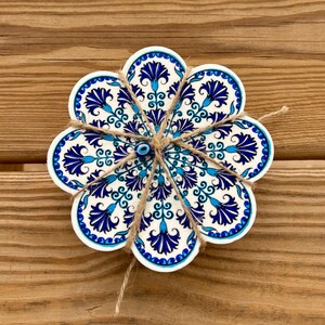 K&ouml;nnte beinhalten: Ein Set aus sechs blauen und wei&szlig;en Keramik-Untersetzern mit einem Blumenmuster und einem blauen b&ouml;sen Blick-Anh&auml;nger in der Mitte. Die Untersetzer sind mit Schnur zusammengebunden.