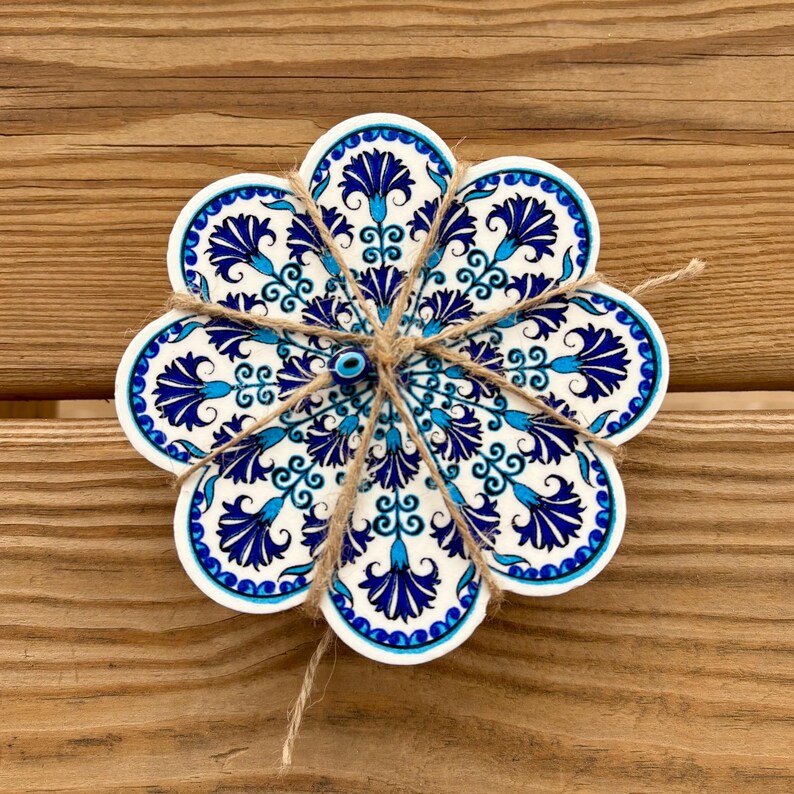 K&ouml;nnte beinhalten: Ein Set aus sechs blauen und wei&szlig;en Keramik-Untersetzern mit einem Blumenmuster und einem blauen b&ouml;sen Blick-Anh&auml;nger in der Mitte. Die Untersetzer sind mit Schnur zusammengebunden.