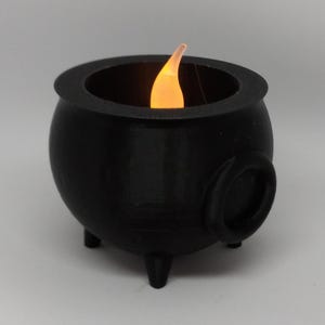 May include: A black cauldron with a small, flickering flame inside. The cauldron has three legs and a handle on the side.