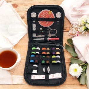 May include: A black zippered travel sewing kit with a variety of colored threads, needles, buttons, a thimble, and a measuring tape.