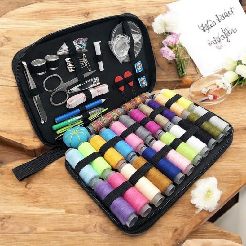 May include: A black zippered case filled with colorful spools of thread, sewing needles, a small pair of scissors, a thimble, and other sewing supplies.