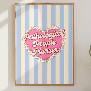 May include: A framed print featuring a pink heart with the words "Pathological People Pleaser" in a retro font. The heart is set against a background of blue and cream vertical stripes. The frame is a light brown color.