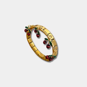 Puede incluir: Pulsera dorada con diseño de eslabones rectangulares. La pulsera presenta dijes de cerezas rojas con hojas verdes. Las cerezas están espaciadas uniformemente alrededor de la pulsera.