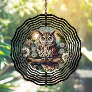 May include: A metal wind spinner with a circular design featuring a detailed illustration of an owl with intricate patterns and a moon in the background. The owl is surrounded by foliage and flowers.