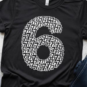 May include: Black t-shirt featuring a large white number six composed of smaller sevens. The design is centered on the shirt, with the number six taking up a significant portion of the front.