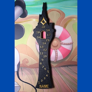 May include: A black tower-shaped countdown board with gold-coloured numbers from 1 to 20 arranged vertically. The structure features a small rectangular cutout near the top, a diamond-shaped gold accent, and the word NAME printed at the base.