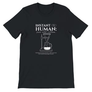 May include: Black t-shirt with white text and a coffee-making illustration. The text reads "INSTANT HUMAN: just add coffee." Below the graphic, it says "Unlocking my human potential a coffee scoop away from transforming groggy into goals."