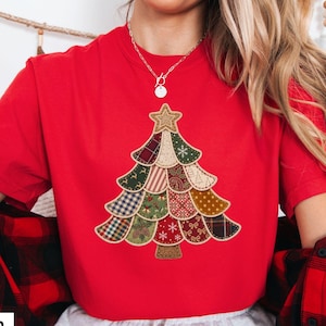 May include: A bright red short-sleeved t-shirt featuring a large, central graphic of a Christmas tree constructed from various patchwork fabric patterns, including plaid, polka dots, snowflakes, and floral designs, topped with a gold star.