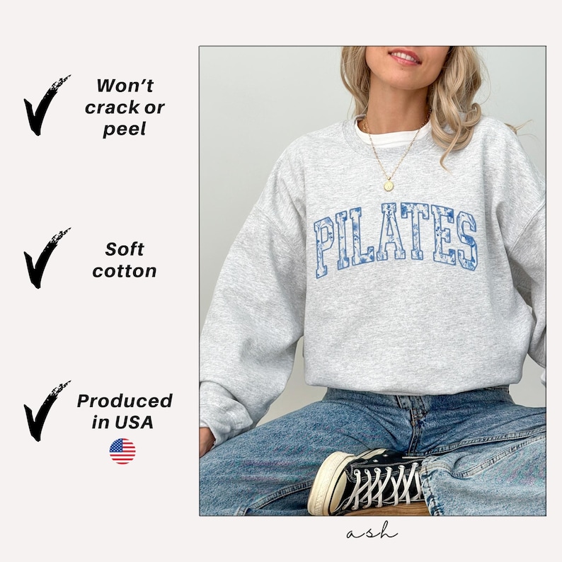 May include: A light gray Pilates sweatshirt with blue floral lettering. The sweatshirt is made of soft cotton and produced in the USA. The text "Won't crack or peel" is also visible.