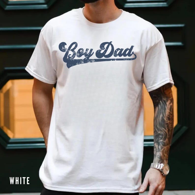 Puede incluir: Camiseta blanca con el texto "Boy Dad" en una escritura azul marino desgastada. La camiseta tiene mangas cortas y cuello redondo. La palabra "WHITE" est&aacute; impresa en la parte inferior de la camiseta.