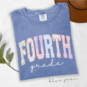 Peut inclure: Un t-shirt bleu délavé à col rond avec une étiquette Comfort Colors. L'avant présente le mot FOURTH en grandes lettres majuscules avec un motif floral et vichy pastel, et le mot grade en écriture cursive blanche juste en dessous.