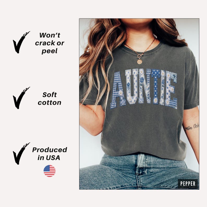 May include: Dark gray t-shirt with the word "AUNTIE" in patchwork letters. The letters are made of blue and white floral and gingham patterns. The shirt is paired with blue jeans. The text "Won't crack or peel", "Soft cotton", and "Produced in USA" are on the left.