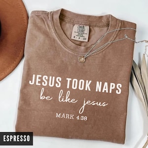 May include: Espresso-colored t-shirt with the text "JESUS TOOK NAPS be like jesus MARK 4:38" in white. The shirt has a crew neck and a small tag on the upper back. A silver necklace with a pendant is draped across the shirt.
