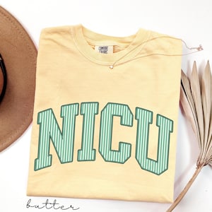 May include: A butter yellow short-sleeve t-shirt with a crew neckline and the text NICU printed in large, green and white vertical striped block letters across the chest. The shirt features a Comfort Colors brand label at the inner neck.