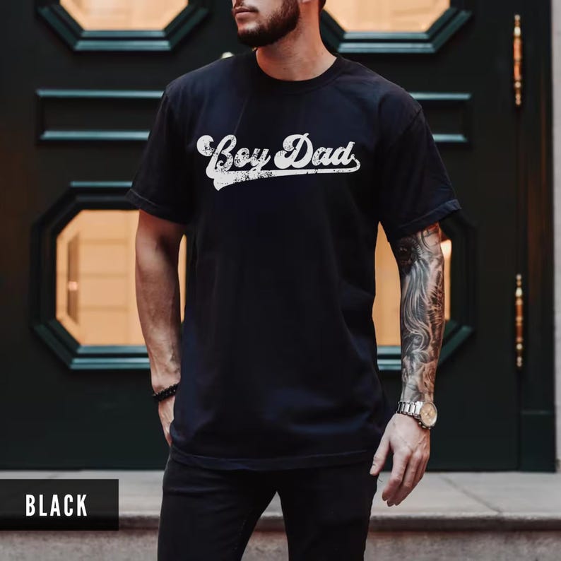 Puede incluir: Camiseta negra con la frase "Boy Dad" en blanco, con un dise&ntilde;o desgastado. La camiseta es de cuello redondo y parece estar hecha de un material suave. La palabra "BLACK" est&aacute; en la parte inferior de la imagen.