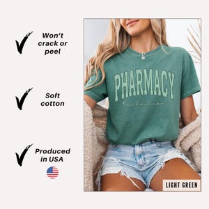 K&ouml;nnte beinhalten: Ein hellgr&uuml;nes Kurzarm-T-Shirt mit dem Text PHARMACY in einer gro&szlig;en, geschwungenen, gestreiften Schriftart und dem Wort technician in einer kleineren Schreibschrift darunter. Das Shirt wird mit hellblauen Jeansshorts und einer beigen Strickjacke kombiniert.