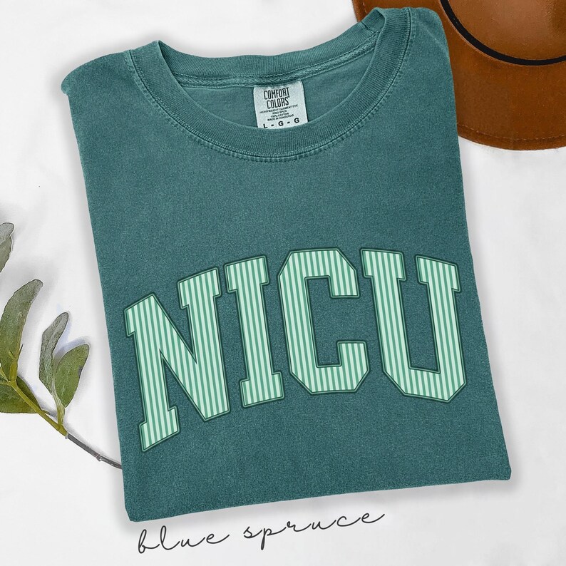 May include: A teal short-sleeve t-shirt with a crew neckline. The front features the text NICU in large, block-style letters with a light green and white vertical striped pattern. The shirt has a Comfort Colors brand label at the neck.