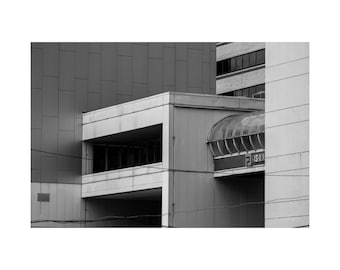 May include: Black and white architectural photograph of a building with geometric shapes. The image features a rectangular structure with a balcony, a curved glass walkway, and the word "FASHION" visible.