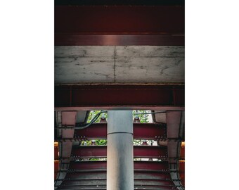 May include: An architectural perspective featuring a concrete ceiling and a series of red metal beams. A cylindrical concrete pillar supports the structure, with glimpses of greenery visible between the beams. The image has a modern, industrial aesthetic.