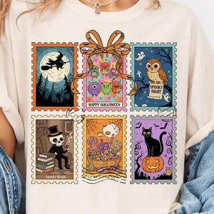 Op de afbeelding: Crèmekleurig T-shirt met zes Halloween-thema postzegelontwerpen. De postzegels tonen een vliegende heks, een uil, een skelet, een zwarte kat op een pompoen en andere griezelige illustraties. De woorden "Happy Halloween" en "Spooky Night" zijn ook zichtbaar.