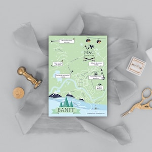May include: A light green illustrated map of Banff, Canada, with a blue ribbon banner that reads "BANFF". The map shows various landmarks, including the Fairmont Banff Springs Hotel, the Banff Gondola, and the Buffalo Mountain Lodge. The map also includes the text "M&C" and "August 11, 2018".