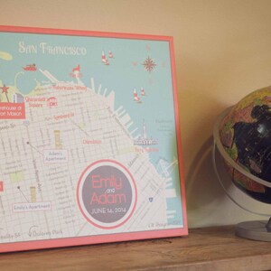 May include: A pink and white map of San Francisco with the text "Emily and Adam" and "June 14, 2014" printed on it. A globe with a black and white map is in the background.