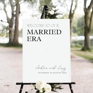 May include: White wedding welcome sign with black text that reads "Welcome to our Married Era" and "Andrea and Larry" with the date "Saturday 24 August 2025".