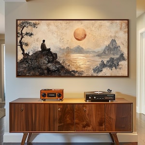 May include: A framed landscape painting depicts a person meditating on a rock, with a tree, mountains, and a large sun. A wooden cabinet with a vintage radio and record player sits below the artwork.