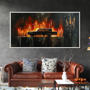 May include: An abstract painting in a white frame depicts a black car surrounded by flames and candles. The artwork has a dark, dramatic color palette with shades of red, orange, and black, creating a mysterious atmosphere. The painting is displayed above a brown leather sofa.