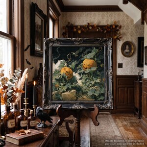 May include: A square painting in an ornate black frame depicting two carved orange jack-o'-lanterns nestled among green pumpkin vines and leaves against a dark, moody background. The artwork features a textured, painterly style with visible brushstrokes.
