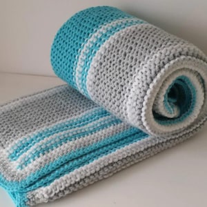 May include: A soft, striped crocheted blanket in shades of gray, white, and turquoise. The blanket is rolled up, showing the different colors and textures.