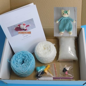 May include: A craft kit in a cardboard box, containing a crochet cat doll, yarn, stuffing, and a pattern. The kit includes blue and white yarn, a crochet hook, and small accessories. The pattern is labeled "DOMINOMB KIT PATTERN."