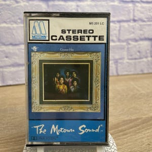 May include: A vintage Motown stereo cassette tape. The cassette features a blue and gold design with the text "STEREO CASSETTE" and "Greatest Hits." The cover art displays a framed photograph of a group of people. The text "The Motown Sound" is also visible.